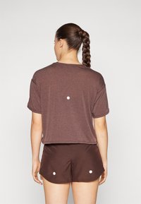 Camisa marrón de manga corta con un ajuste relajado, que presenta un escote redondo y un detalle circular en la parte posterior. Combinada con pantalones cortos marrones a juego.
