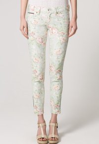 Jeans skinny de estampado floral en verde menta claro con rosas rosas. Presenta una cremallera en los tobillos y detalles sutiles de desgaste.