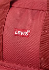 Gros plan d'un sac en tissu rouge présentant un patch logo Levi's cousu en blanc et rouge.