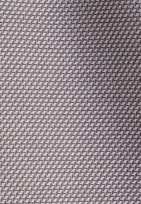 Gros plan d'un tissu texturé avec un motif chevron diagonal répétitif en tons gris clair et foncé.