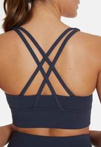 Navy sportbeha met een crisscross bandontwerp op de rug, gemaakt van gladde, rekbare stof met een aansluitende pasvorm.
