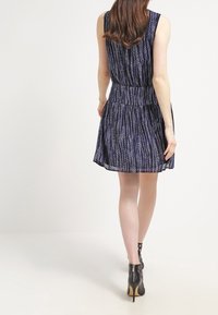 Navyblaues ärmelloses Kleid mit vertikalen weißen Mustern, tailliert und mit schwingendem Rock. Die Rückansicht zeigt eine glatte Textur und einen leichten Stoff.