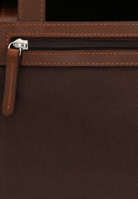 Primo piano di tessuto marrone scuro con cerniera orizzontale in metallo e rifinitura e tiretto in pelle marrone.