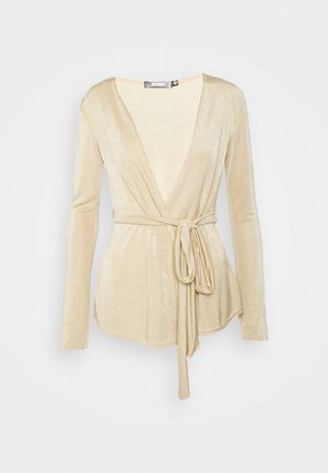 Haut cache-cœur doré à manches longues en tissu doux et brillant avec un décolleté en V profond et une ceinture nouée à la taille. Texture lisse, design décontracté.