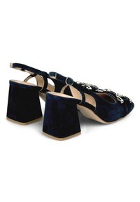 Sandali con tacco a blocco in suede blu navy, con punta aperta, cinturino alla caviglia regolabile e decorazione in catena metallica sulla parte anteriore.