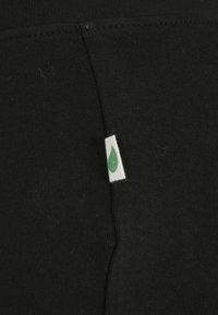 Tissu noir avec une petite étiquette blanche avec un symbole de feuille verte cousue dans une couture.