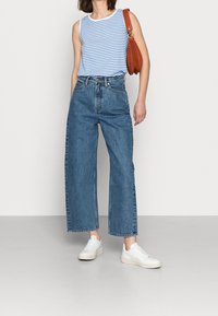 Blå och vit randig linne, högmidjade vida jeans, vita sneakers och en brun axelväska.