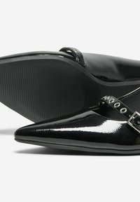 Ballerines Mary Jane noires en cuir verni à bout pointu avec une boucle en argent et des détails en œillets, une chaussure montrant une semelle texturée.