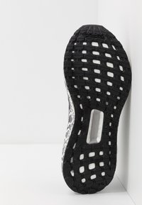 Suela de zapatilla de patrón en blanco y negro con goma texturizada, diseño de banda de rodadura hexagonal y una unidad de amortiguación visible en la mediasuela.