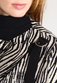 Stickad tröja med ett djärvt svart och vitt zebrarandigt mönster, med en texturerad yta och en svart rem försedda med en silverring.