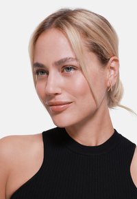Top senza maniche a coste nere con collo alto, indossato da una persona con capelli biondo chiaro e orecchini a cerchio di argento minimal.