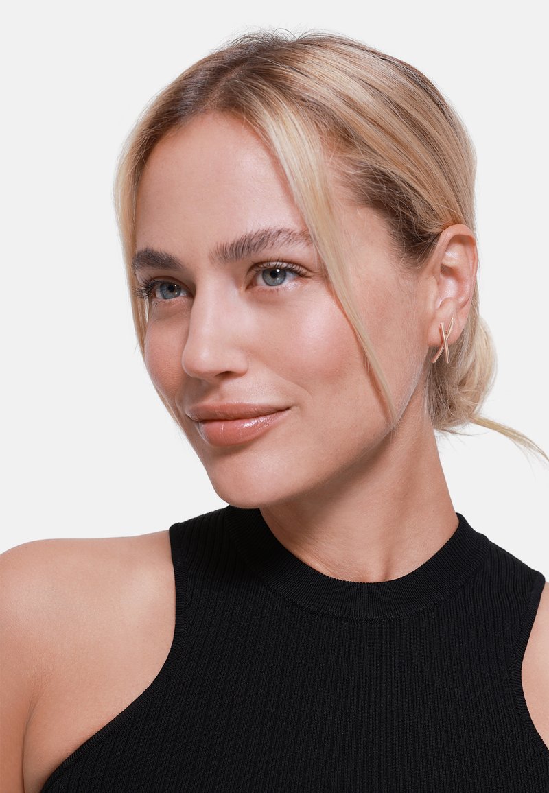 Top senza maniche a coste nere con collo alto, indossato da una persona con capelli biondo chiaro e orecchini a cerchio di argento minimal.