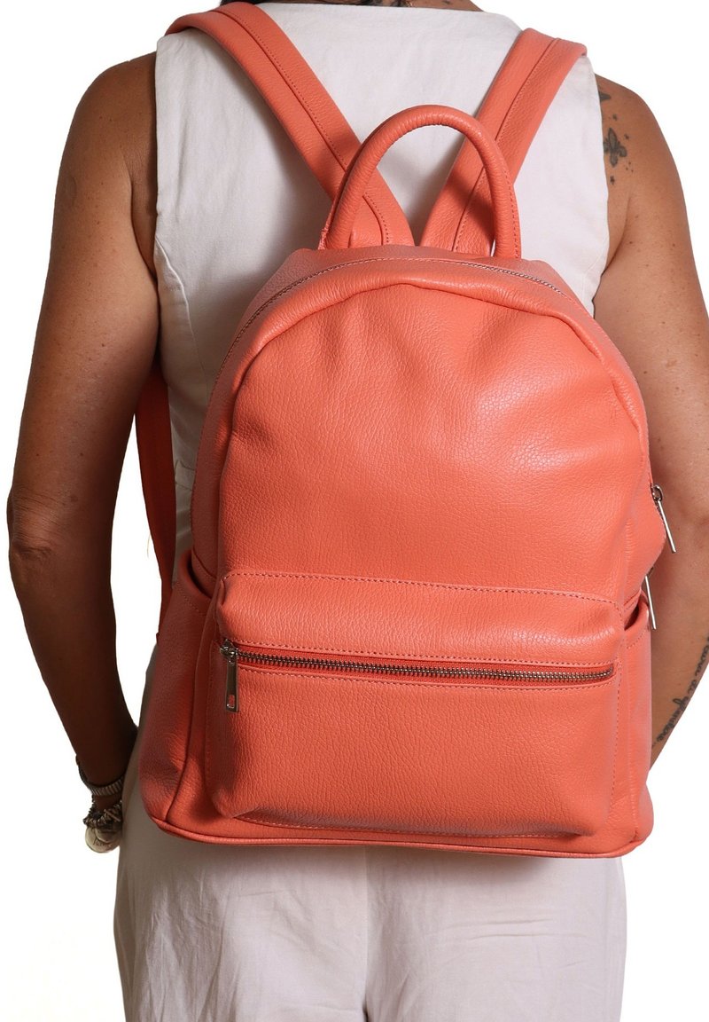 Sac à dos en cuir corail avec une forme arrondie, finition texturée, une poignée supérieure unique et une poche zippée à l'avant. Bretelles réglables.