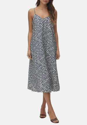 Mujer con vestido midi sin mangas con estampado de hojas en azul marino y blanco y tirantes finos, combinado con tacones negros de tiras.