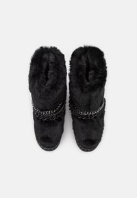 Une paire de bottines noires en fausse fourrure avec des orteils ronds et des chaînes décoratives noires et argentées sur le devant, vues d'en haut.