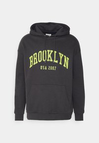 Sudadera negra con capucha y un bolsillo frontal, con texto destacado en amarillo verdoso que dice "BROOKLYN USA 2007" en un estilo vintage.