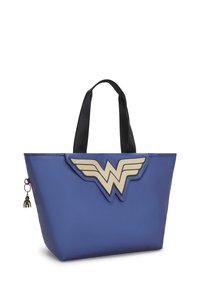 Blå tote-väska med en gyllene Wonder Woman-emblem, svarta handtag och en liten charm-nyckelring. Slät textur, strukturerad form.