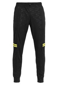 Svarta träningsbyxor med ett subtilt, genomgående logomönster, elastisk midja och en gul accentpatch på vänster ben. Mjuk tygkänsla.