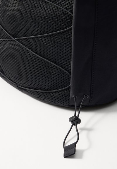 Sac à dos noir avec un panneau en maille texturée, une forme courbée, un cordon de serrage ajustable et des détails de couture élégants.
