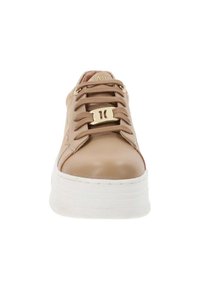 Zapatilla de cuero beige con puntera redondeada, que presenta un acento dorado en la zona de los cordones y una suela blanca gruesa. Parte superior texturizada con costuras detalladas.