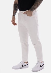 Pantaloni in denim bianco con una vestibilità slim, dettagli leggermente distressed, tasche anteriori e una chiusura classica con bottone e zip.