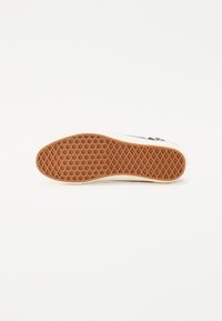 Baskets blanches avec une semelle en caoutchouc présentant un motif en diamant et un accent beige. La tige est en tissu avec des détails graphiques noirs.