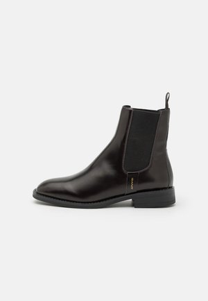 Brown leather Chelsea boot with elastic side panels, rounded toe, and a low block heel; features gold branded tag on side.