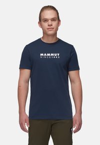Mørkeblå kortærmet t-shirt lavet af bomuld, med et hvidt "MAMMUT SINCE 1862" logo på forsiden. Rund halsudskæring, tætsiddende design.