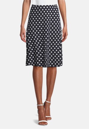 Vrouw met een knielange marineblauwe rok met witte stippen en witte sandalen met hoge hakken en enkelbandjes.