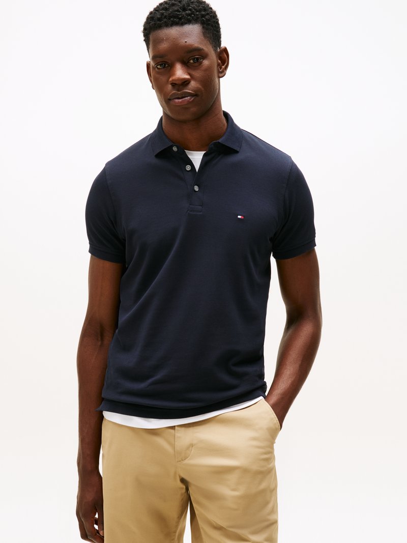 Mørkeblå poloskjorte med klassisk krage, korte ermer og en liten logo på venstre bryst; kombinert med beige bukser.