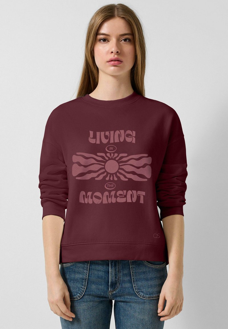 Sweatshirt bordeaux à col rond et manches longues, avec un design graphique central comprenant le texte "VIVRE L'INSTANT".