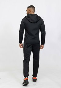 Survêtement de sport noir au design ajusté. Comprend une capuche, des manches longues et un pantalon fuselé. Accentué par des touches d'orange sur les chaussures.