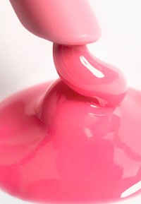 Pink nail polish drips from a finger, showcasing a glossy finish and smooth texture against a white background.