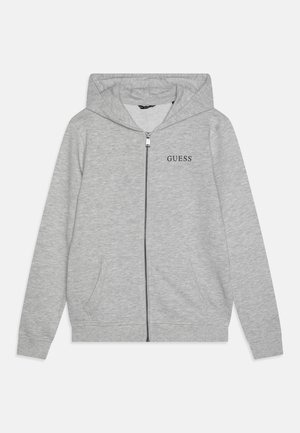 Felpa grigia con zip e cappuccio regolabile, tasche frontali e logo "GUESS" nero sul lato sinistro del petto. Realizzata in tessuto morbido.