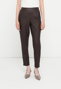 Pantalones marrones ajustados con una textura suave, que presentan pliegues frontales y una cinturilla plana. Combinados con unos zapatos planos beige de punta afilada.