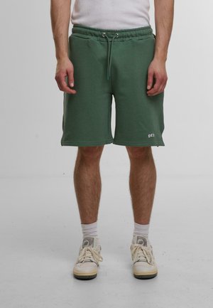 Grønne svedshorts lavet af en bomuldsblanding, med justerbar snøre i taljen, sidelommer og et lille logo på den nederste kant.