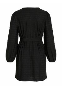 Vestido negro con mangas largas y abullonadas, que presenta una tela texturizada y una cintura ceñida con cinturón, visto desde atrás.