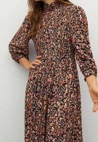Robe fleurie avec un corsage froncé, un col montant et des manches longues bouffantes. Fond sombre avec des motifs floraux orange et rose.