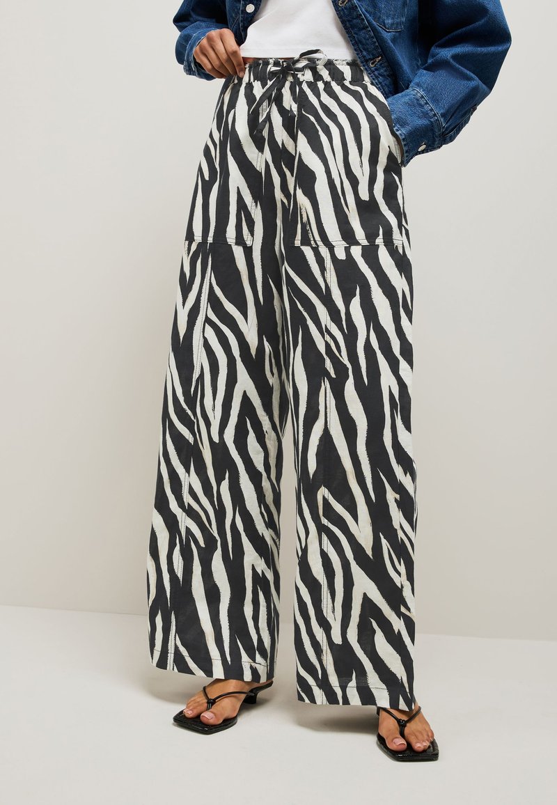 Person wearing black and white zebra print wide-leg pants, white top, denim jacket, and black strappy sandals with square toes.