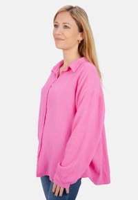 Leuchtend pinkes Hemd mit Knopfleiste aus strukturiertem Stoff, lockerer Passform und langen Ärmeln, kombiniert mit Jeans.