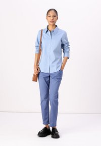 Lyseblå skjorte med knappestolpe og lange ermer som er rullet opp ved mansjettene, sammen med lyseblå bukser. Svarte platåsko og en brun crossbody-veske.