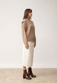 Lichtroze gebreide trui met een hoge hals, gecombineerd met een witte linnen rok en bruin leren enkellaarsjes met blokhak.