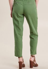 Groene linnen broek met een tapse pasvorm, elastische tailleband en achterzakken; gecombineerd met bruine haksandalen.