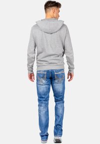 Grijze hoodie met een trekkoord, gecombineerd met lichtblauwe denim jeans met gedetailleerde stiksels en een slim fit. Witte sneakers maken de look af.