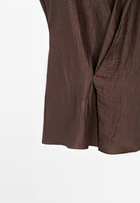 Brown textured fabric draped with a twisted knot detail, showing a close-up of soft, flowy material on a white background.