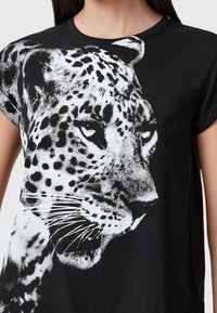 T-shirt noir en coton avec un grand graphique de léopard blanc sur le devant, à manches courtes et col rond.