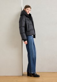 Veste de puffer noire avec capuche, dotée d'une fermeture éclair et de poches latérales. Associée à un jean bleu ample et des bottes à plateforme noires.