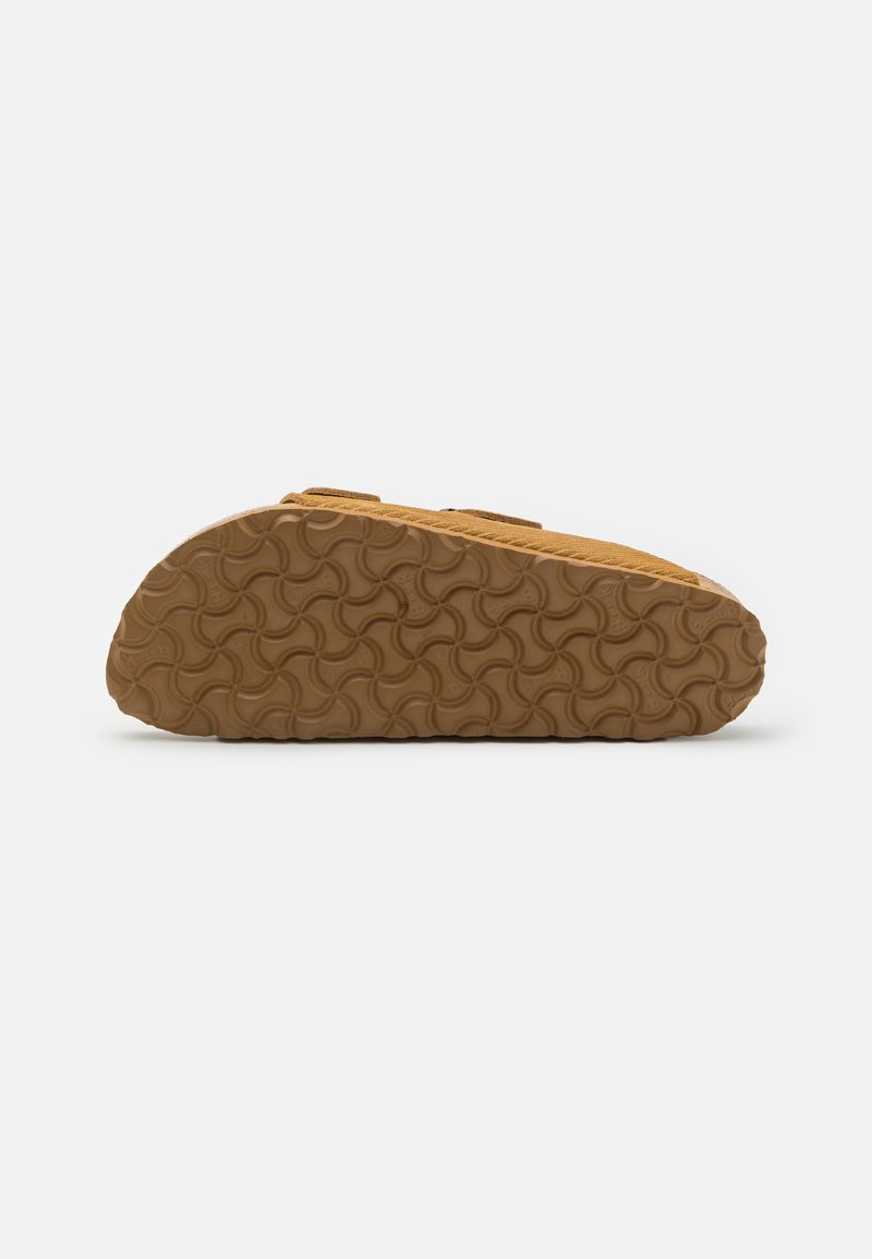 Beige Wildleder Slipper mit einer strukturierten Gummisohle, die ein wellenartiges Muster aufweist, entworfen für Komfort und Haltbarkeit.