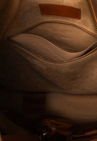 Innenansicht einer braunen Ledertasche mit einem Reißverschluss-Innenfach und aufgenähtem Lederetikett auf weichem Stofffutter.