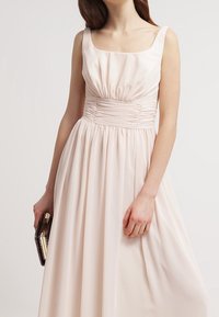 Ljus rosa ärmlös klänning med fyrkantig halsringning, rynkad bodice och flödande kjol, tillverkad av mjukt tyg. Accessoarer med en clutcht väsk.